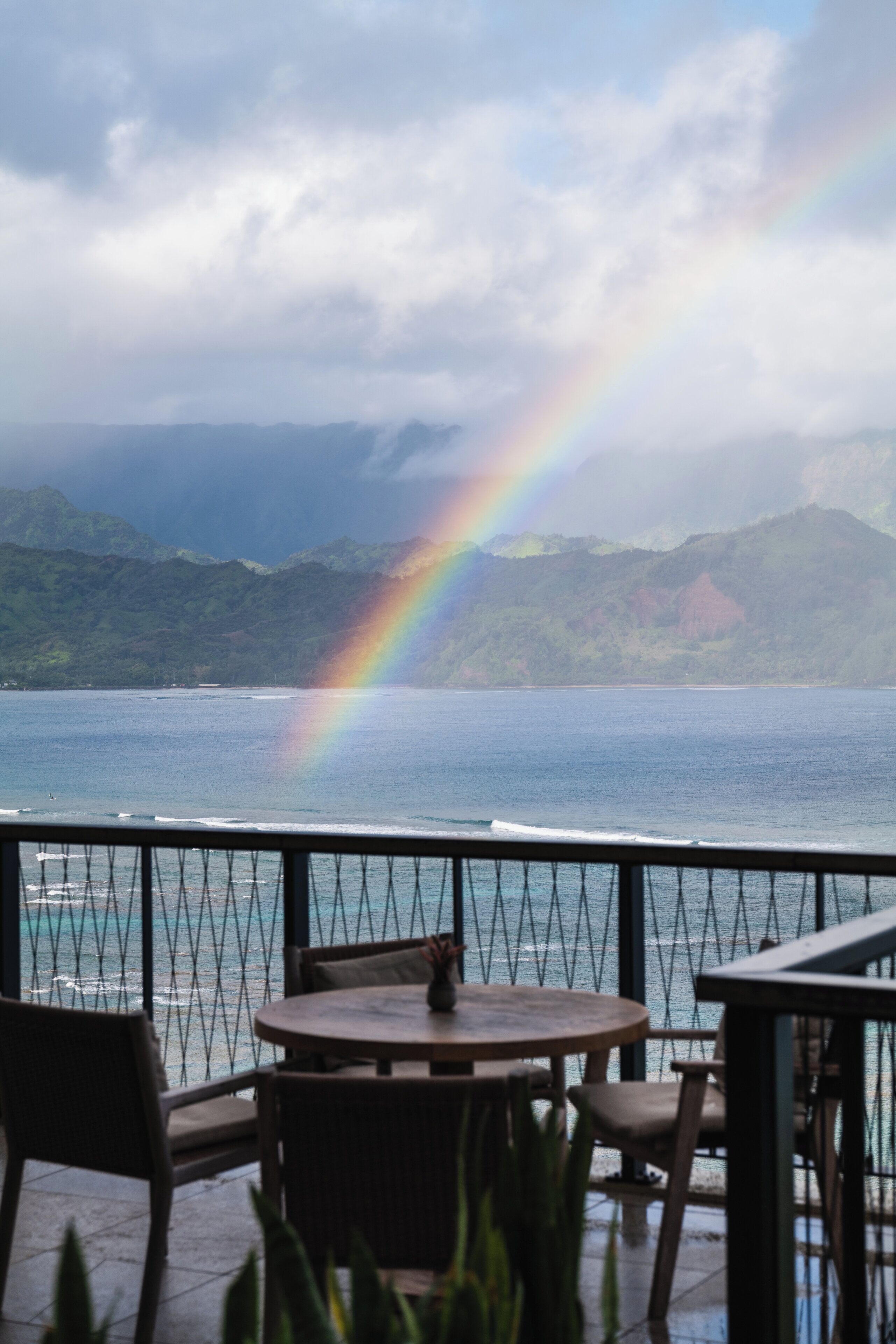 A view from a balcony with a table and chairs, overlooking a body of water and a mountain range.