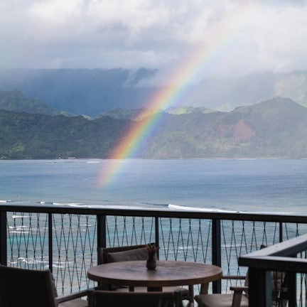 A view from a balcony with a table and chairs, overlooking a body of water and a mountain range.