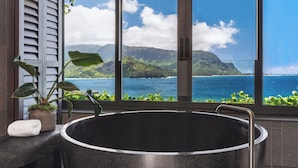 A bathtub with a view of a mountainous landscape and ocean through large windows.