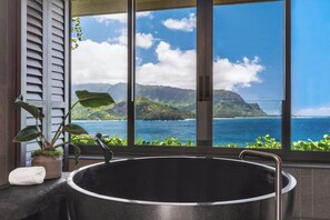 A bathtub with a view of a mountainous landscape and ocean through large windows.