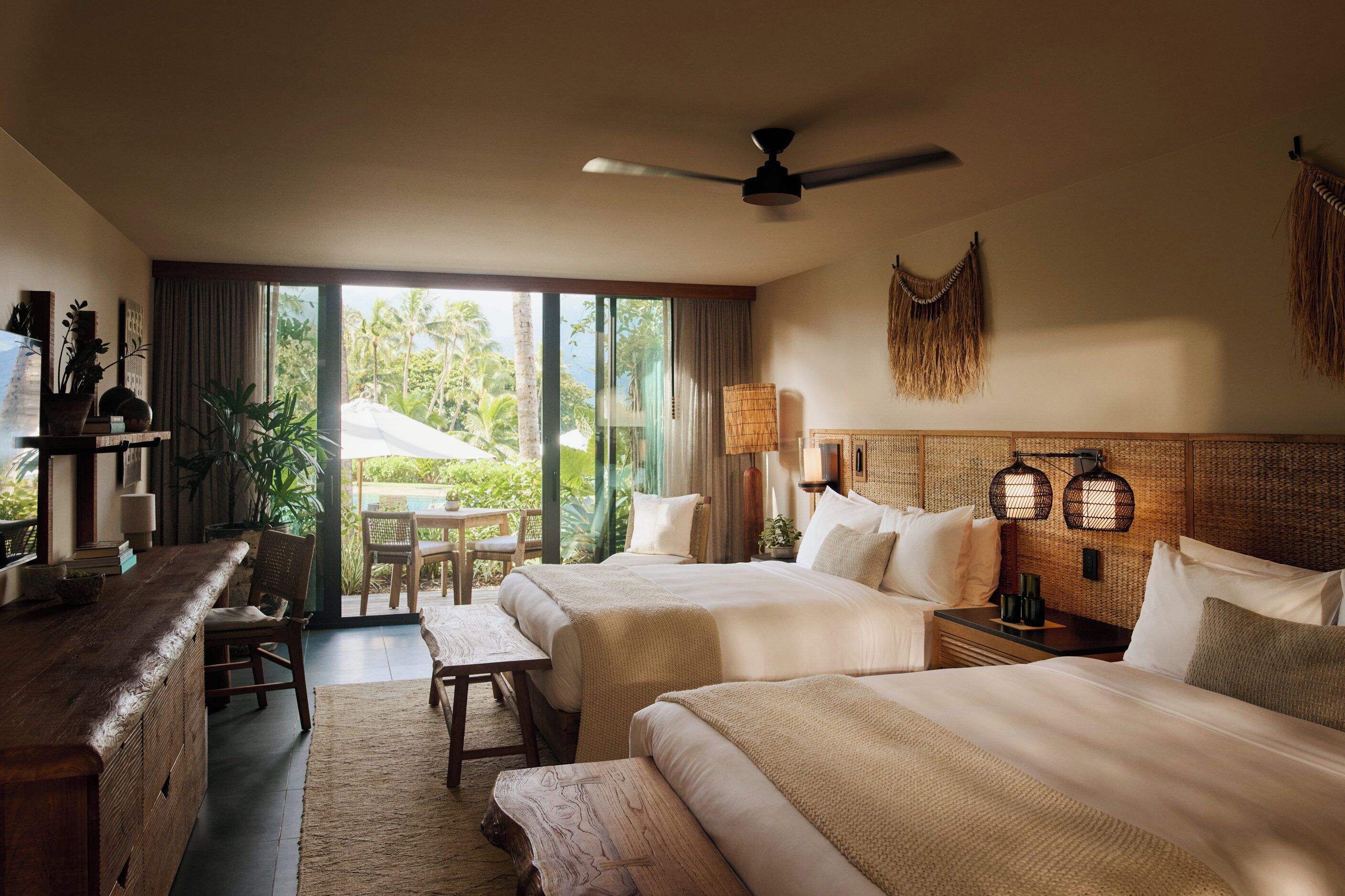 A hotel room with two beds, a desk, a chair, and a view of the outdoors.