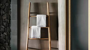A wooden ladder with two white towels against a wall with a stone texture on one side and a dark door on the other.