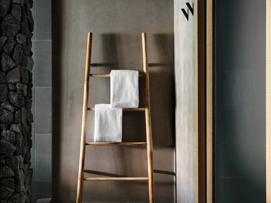 A wooden ladder with two white towels against a wall with a stone texture on one side and a dark door on the other.