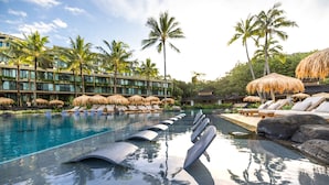 A resort pool with lounge chairs, palm trees, and a building with multiple balconies.
