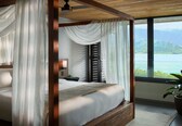 A bedroom with a four-poster bed, sheer curtains, a view of a lake, and a potted plant.