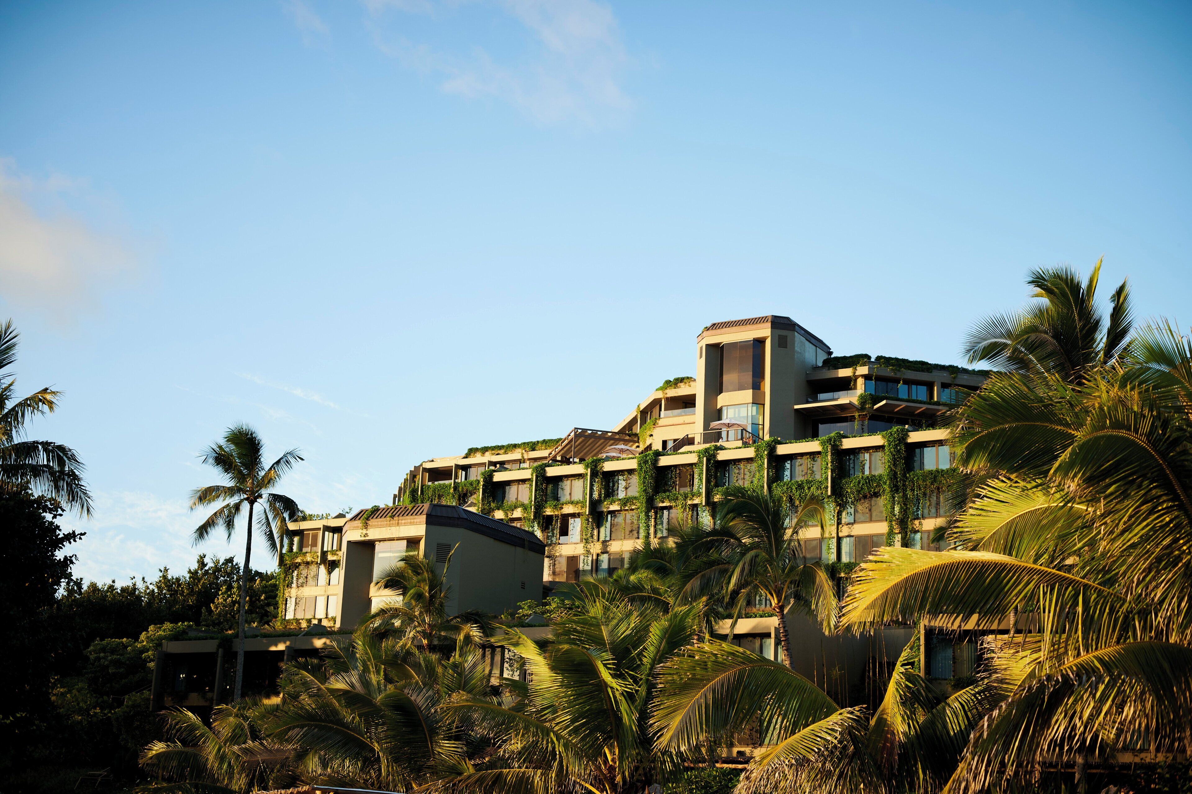 A multi-story hotel with balconies, surrounded by palm trees.