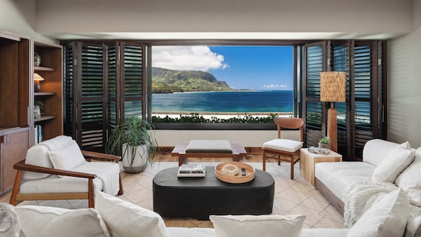 A living room with a view of the ocean, a sofa, a coffee table, and a bookshelf.