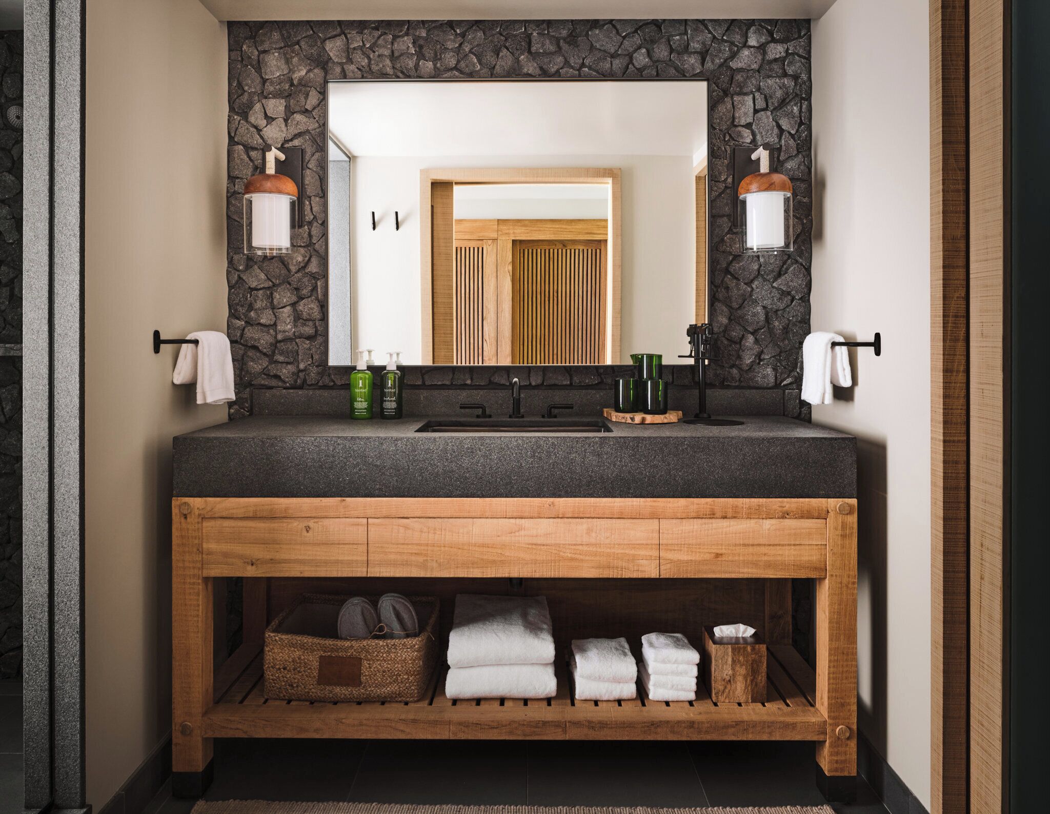 Une salle de bain avec un mur en pierre, un meuble-lavabo en bois et un miroir.