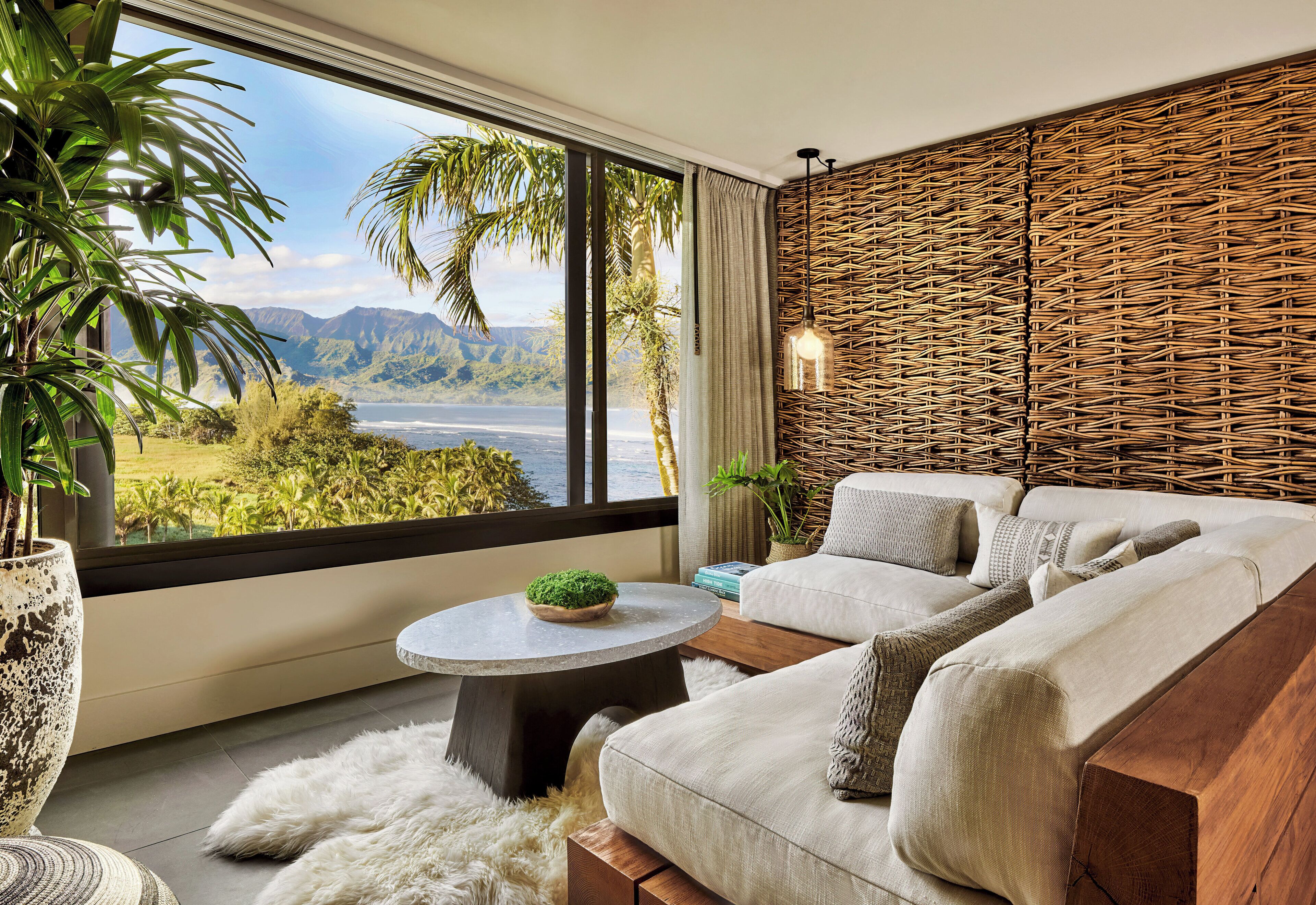 A modern living room with a large window, a sofa, a round coffee table, and a wicker wall panel.