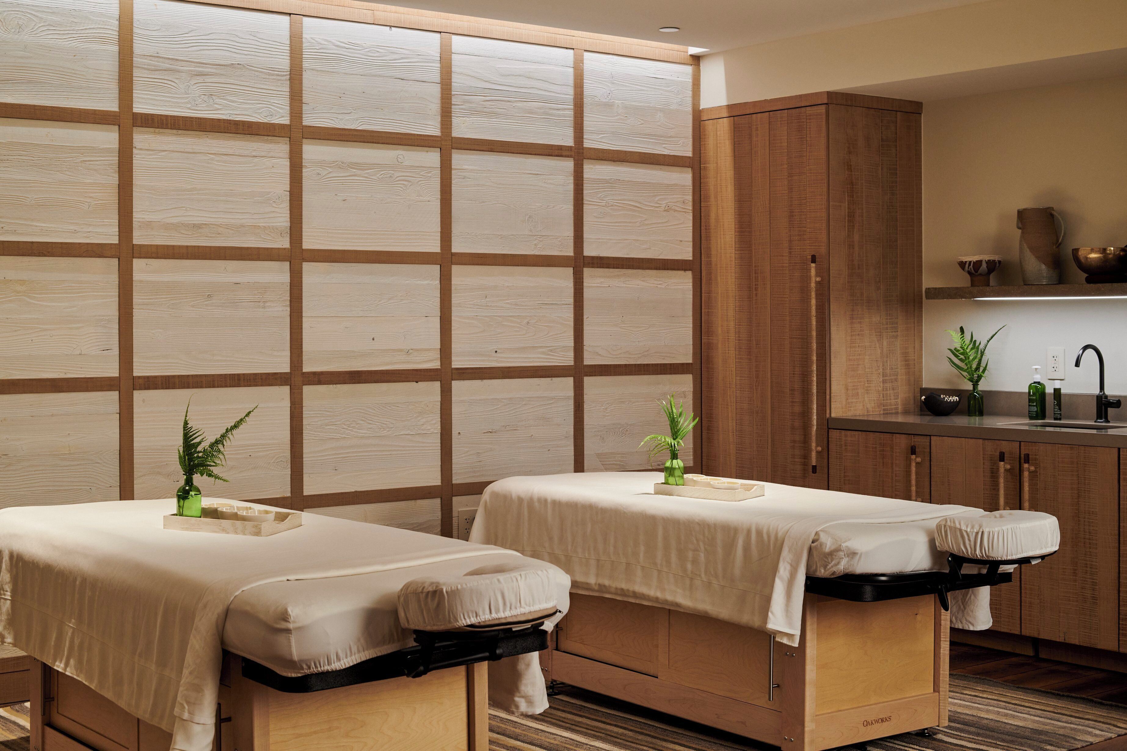 A spa room with two massage tables, a wooden cabinet, and a small kitchenette area.