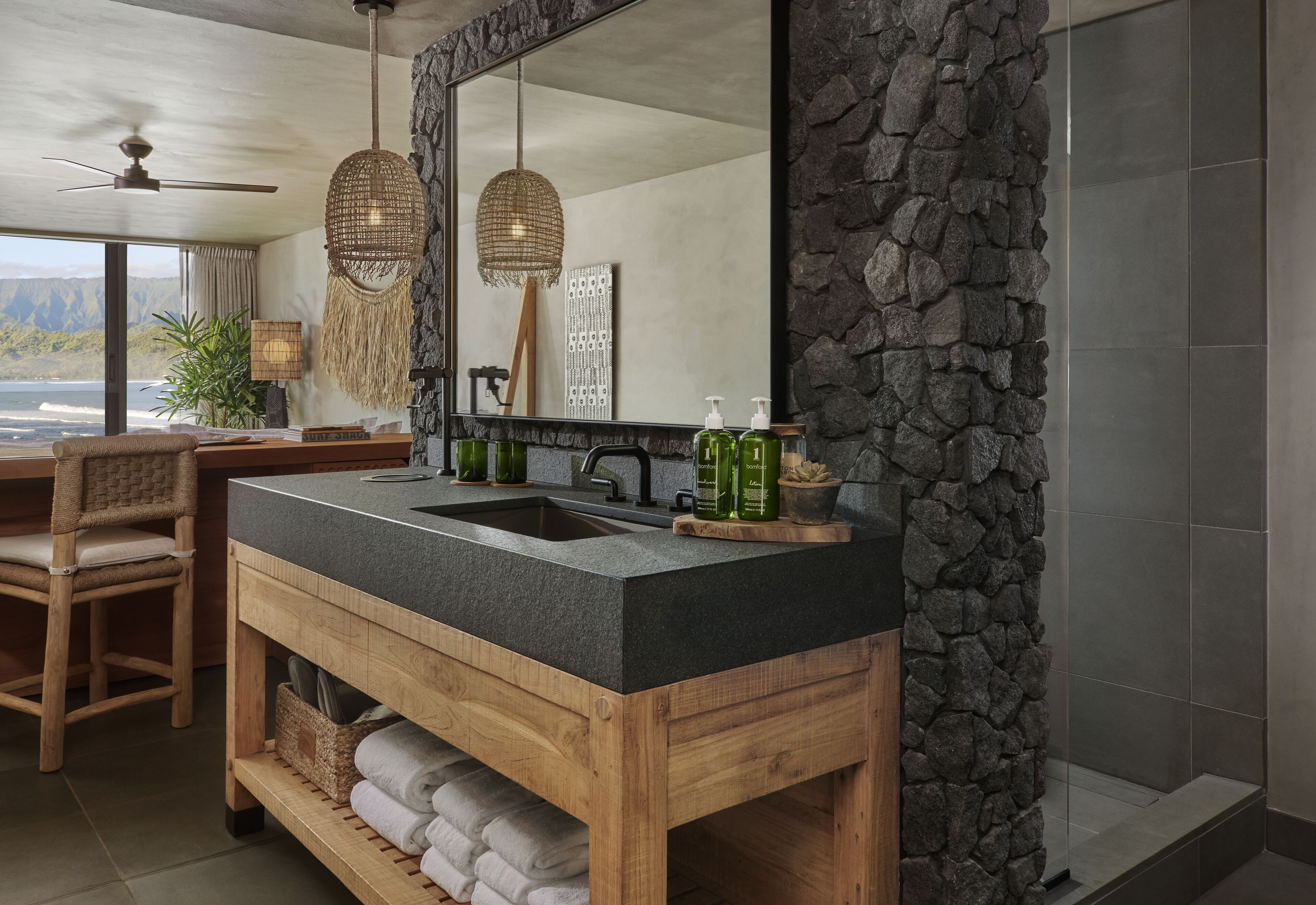 A bathroom with a stone accent wall, a wooden vanity, and a large mirror.