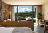 A bedroom with a large bed, a balcony with a view of mountains, and a dining area with a table and chairs.