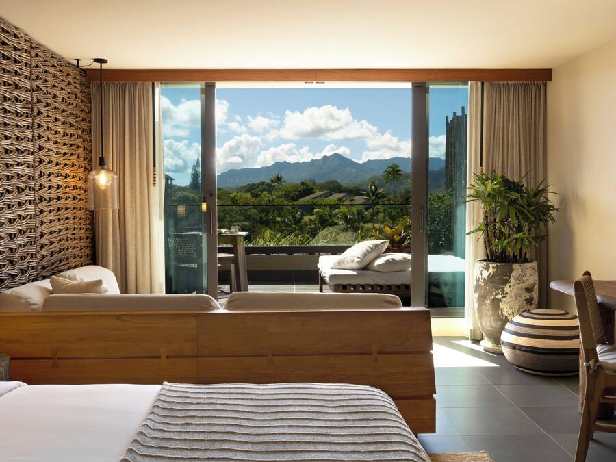 Quarto com cama grande, varanda com vista para montanhas e área de jantar com mesa e cadeiras.