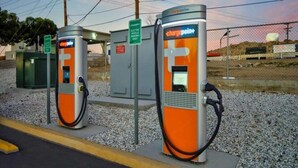 Zwei Ladestationen für Elektroautos mit Zaun und Kiesfläche.