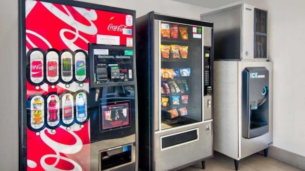 Three beverage vending machines, one with a Coca-Cola logo, another with a variety of snacks, and a third with an ICE dispenser.
