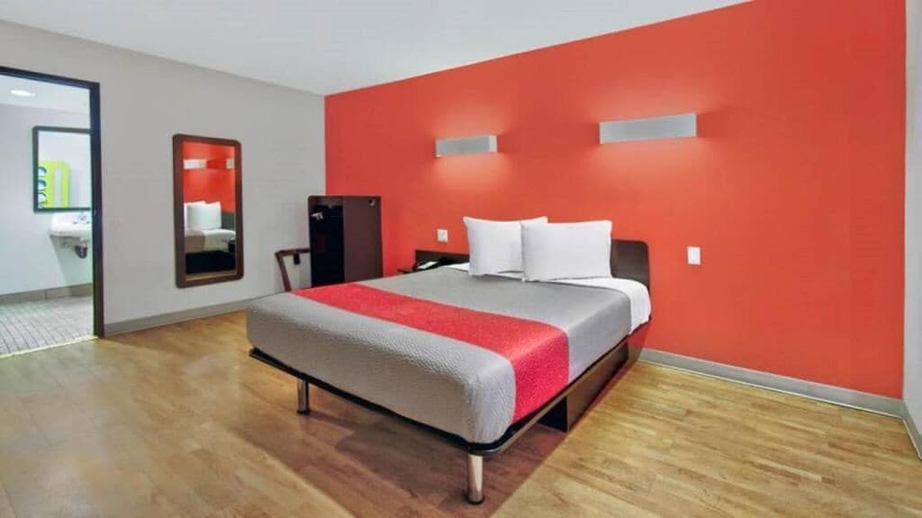 A hotel room with a bed, a desk, a chair, and a mirror.