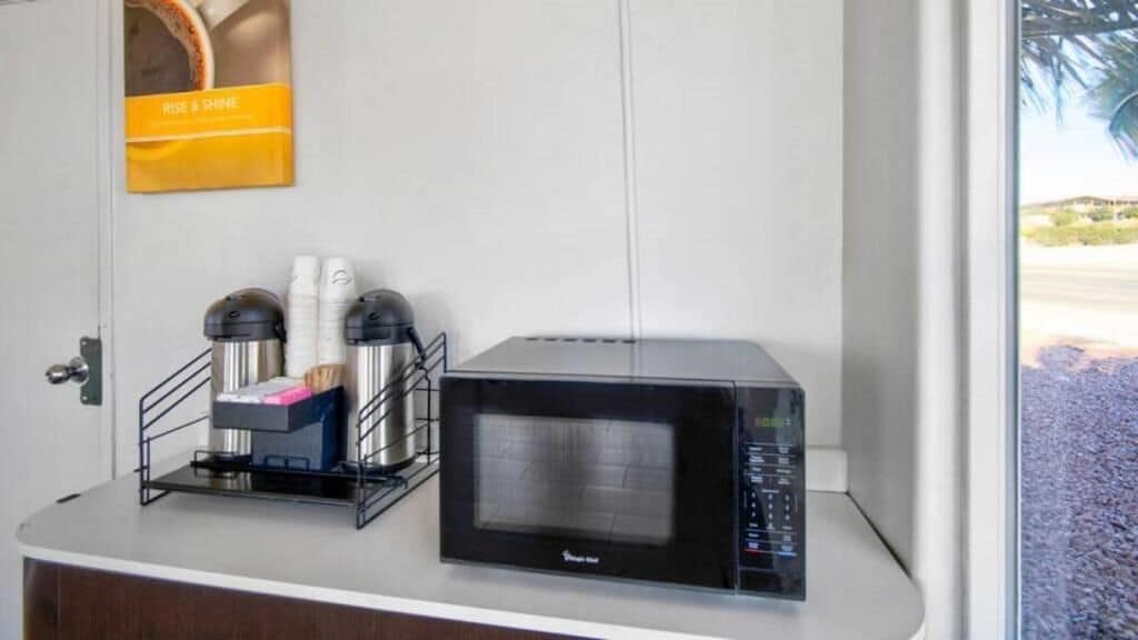 A microwave on a white countertop with a coffee maker and cups on a stand.