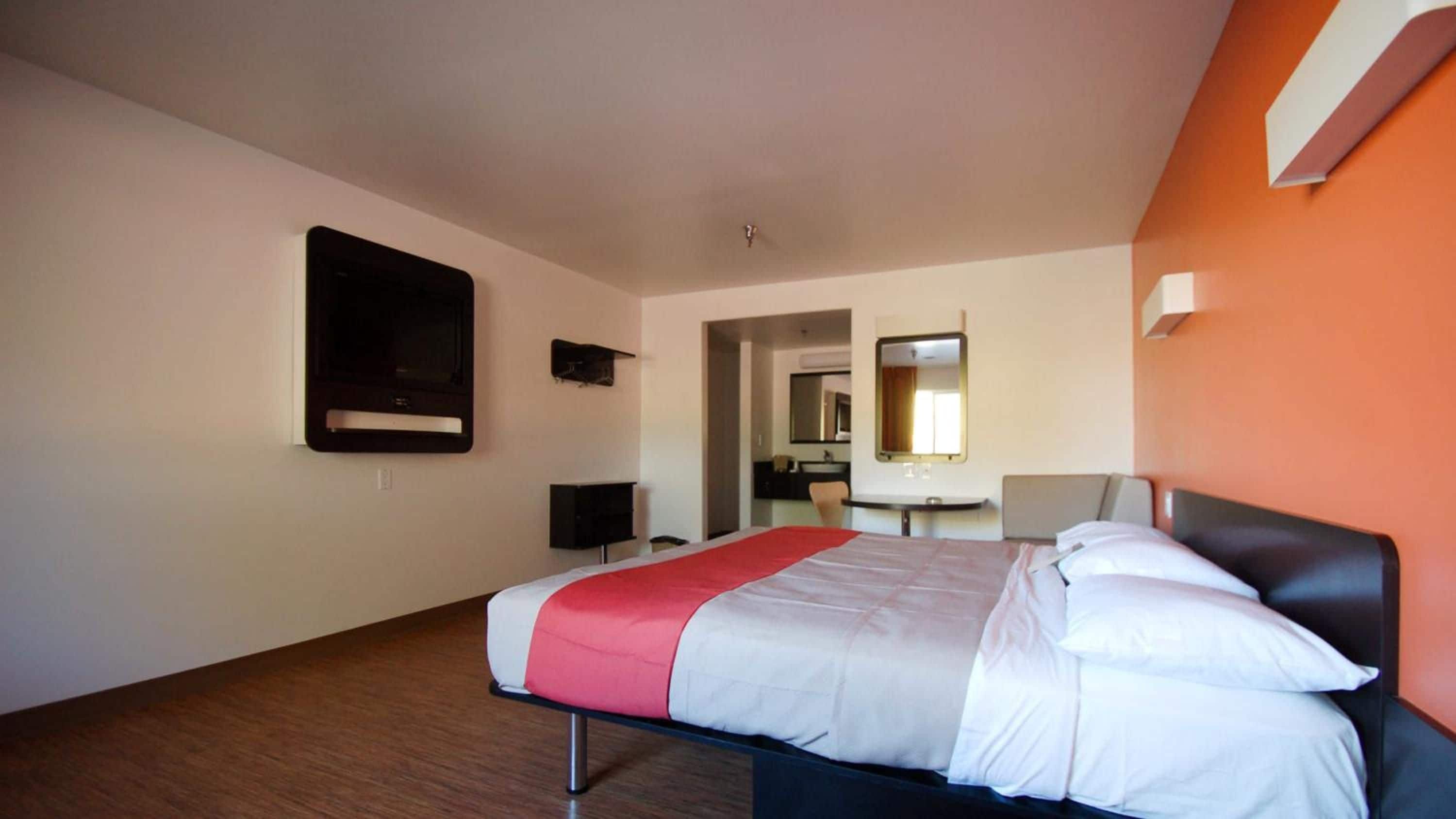 Una habitación de hotel con una cama, televisión, escritorio y espejo.
