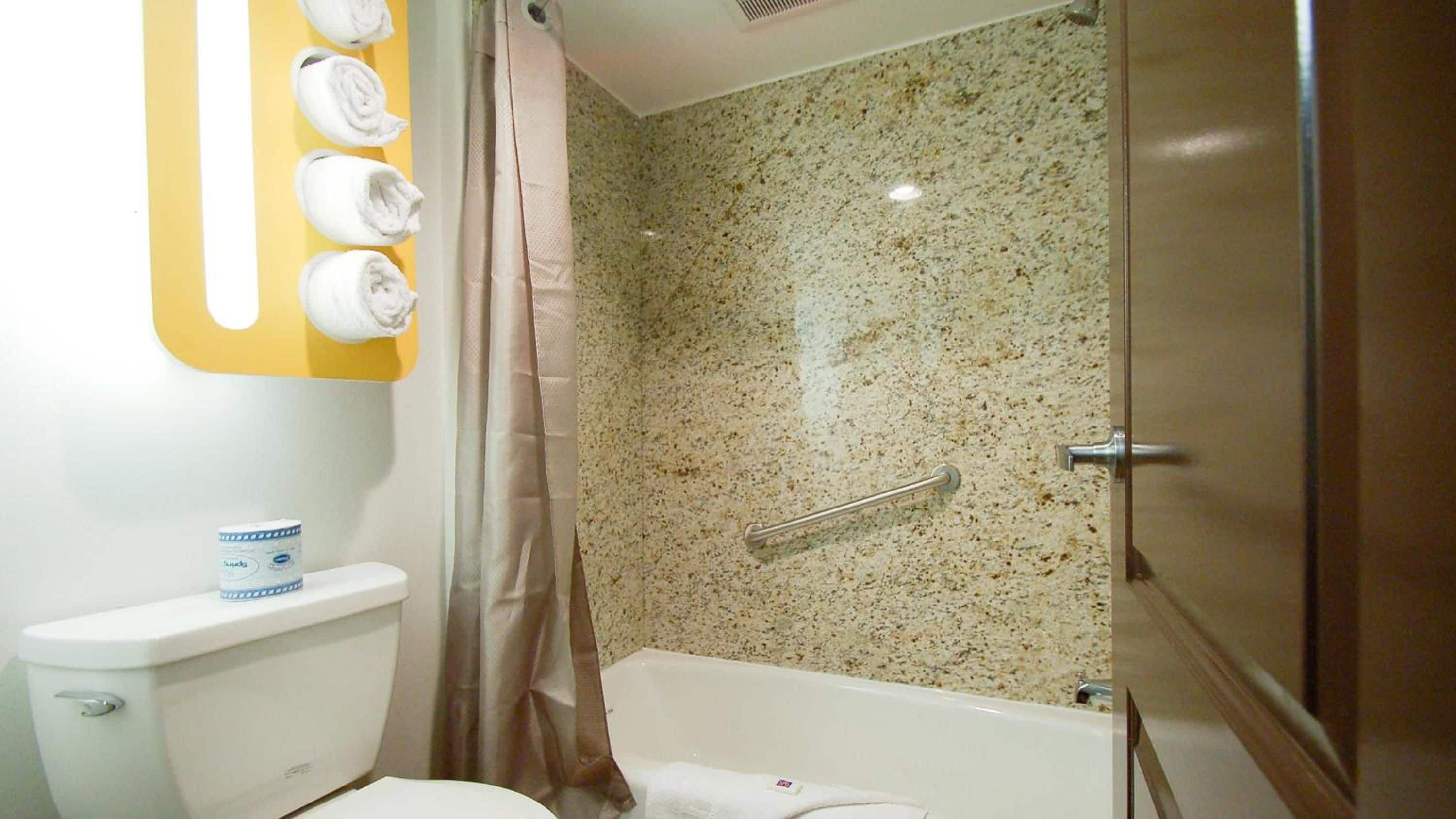 Ein Badezimmer mit Toilette, einer Duschkabine mit Glastür, einem Handtuchhalter mit aufgerollten Handtüchern und einer Wand aus Granit.
