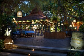 An outdoor restaurant with a traditional roof, tables, chairs, and string lights. - Bumi Surabaya City Resort (Surabaya)