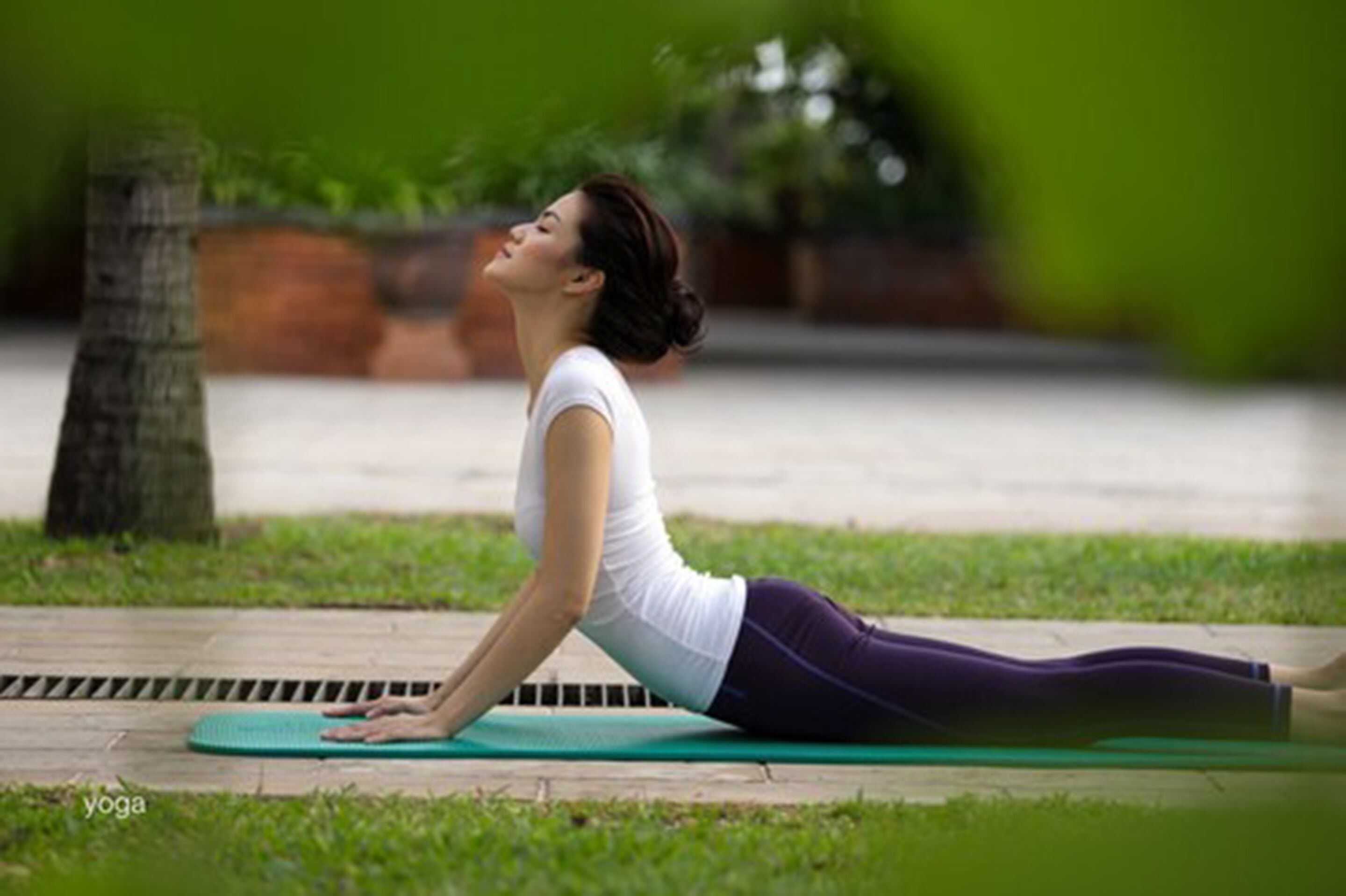 Une personne effectuant une posture de yoga sur un tapis, à l'extérieur.