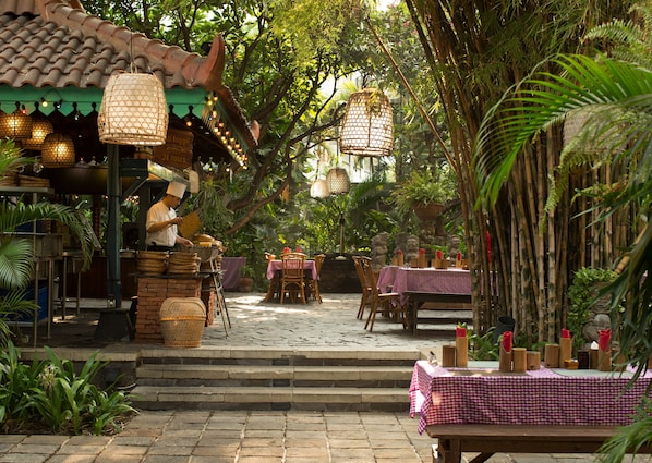 Un restaurant en plein air avec des murs en bambou, des meubles en osier et des lanternes suspendues.