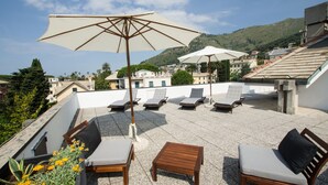 Une terrasse sur le toit, avec des chaises longues, une table en bois et deux parasols.
