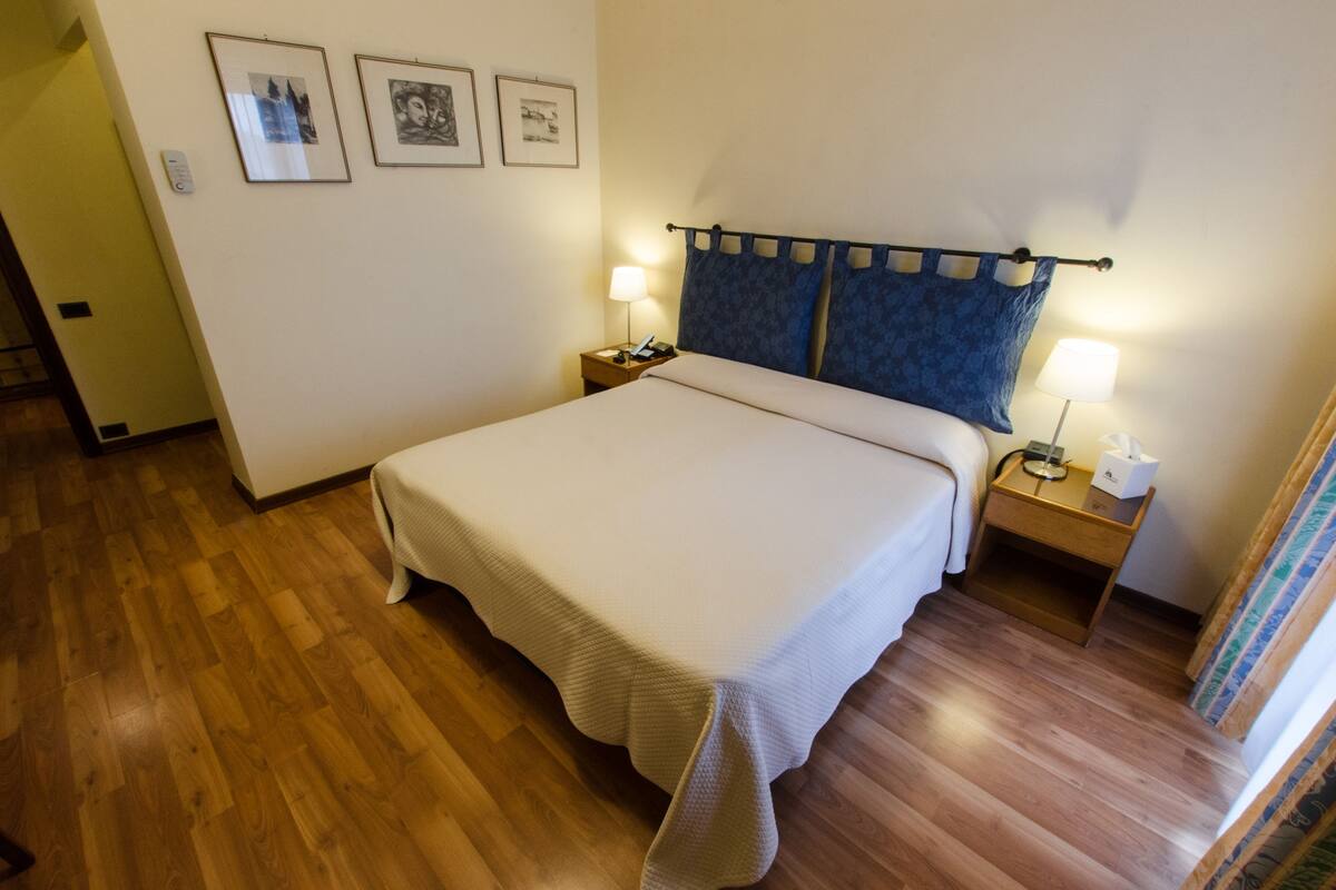 A neatly made bed with a headboard, two bedside tables with lamps, and framed pictures on the wall.
