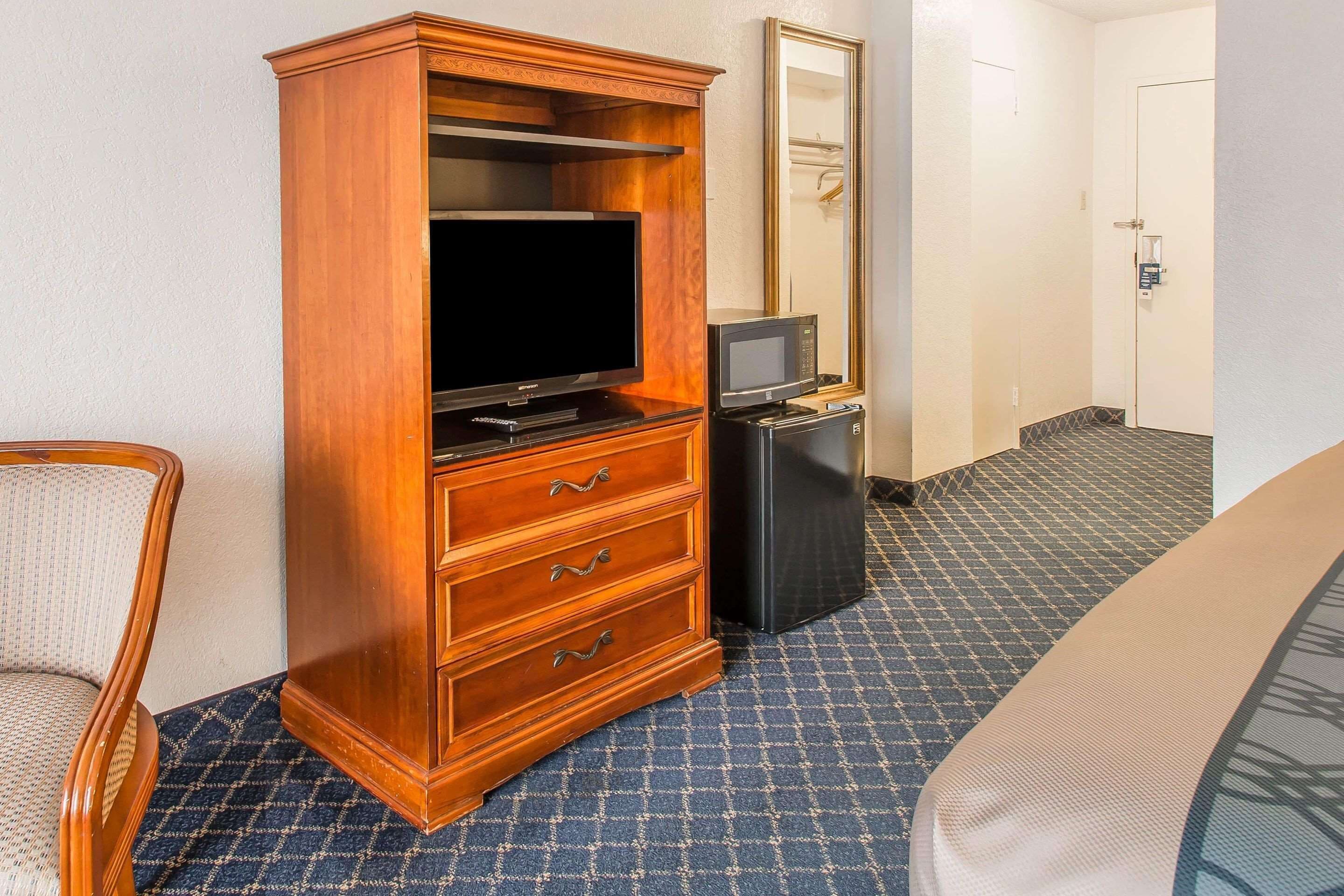 A hotel room with a wooden dresser, a television, a microwave, and a bed.