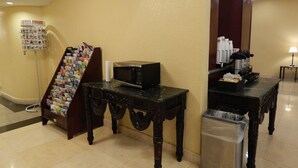 A lobby area with a reception desk, a coffee station, a waste bin, and a magazine rack.