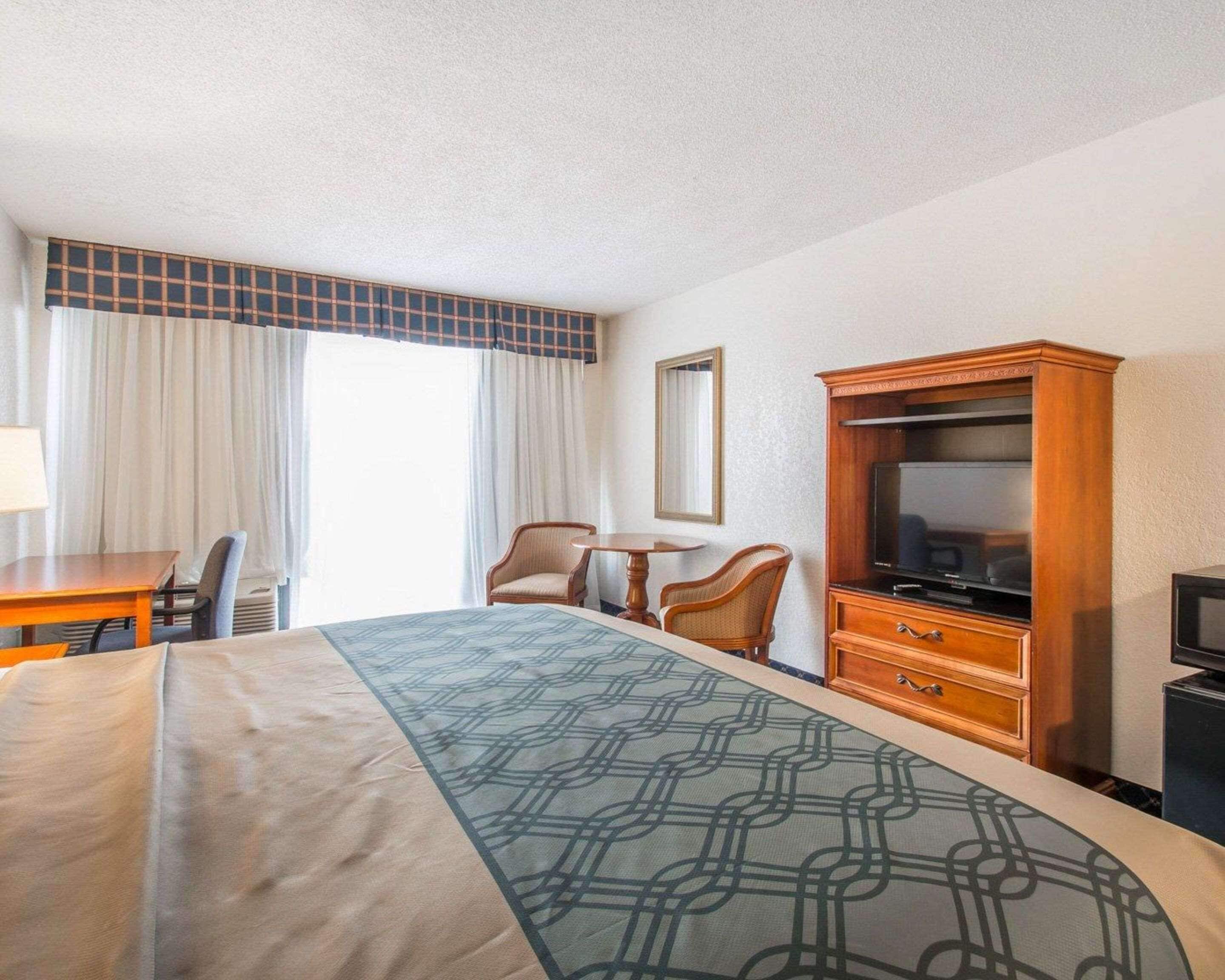 A hotel room with a bed, a desk, two chairs, a television, and a cabinet.
