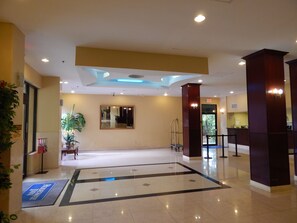 A hotel lobby with a reception desk, a large mirror, and a seating area with a plant. - North Miami Beach Gardens Inn & Suites (North Miami Beach)