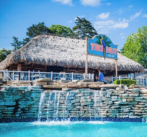 Un edificio con techo de paja y un letrero que dice "TIKI HUT POOL BAR".