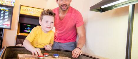 Un hombre y un niño jugando a un juego en una mesa, con una pantalla de fondo.