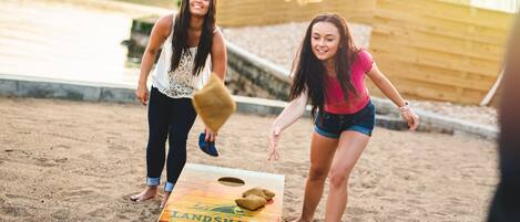 Two people playing a board game on a sandy beach with a wooden board labeled "LANDSHARK."