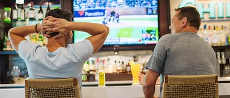 Dos personas sentadas en una barra con un televisor mostrando un evento deportivo.