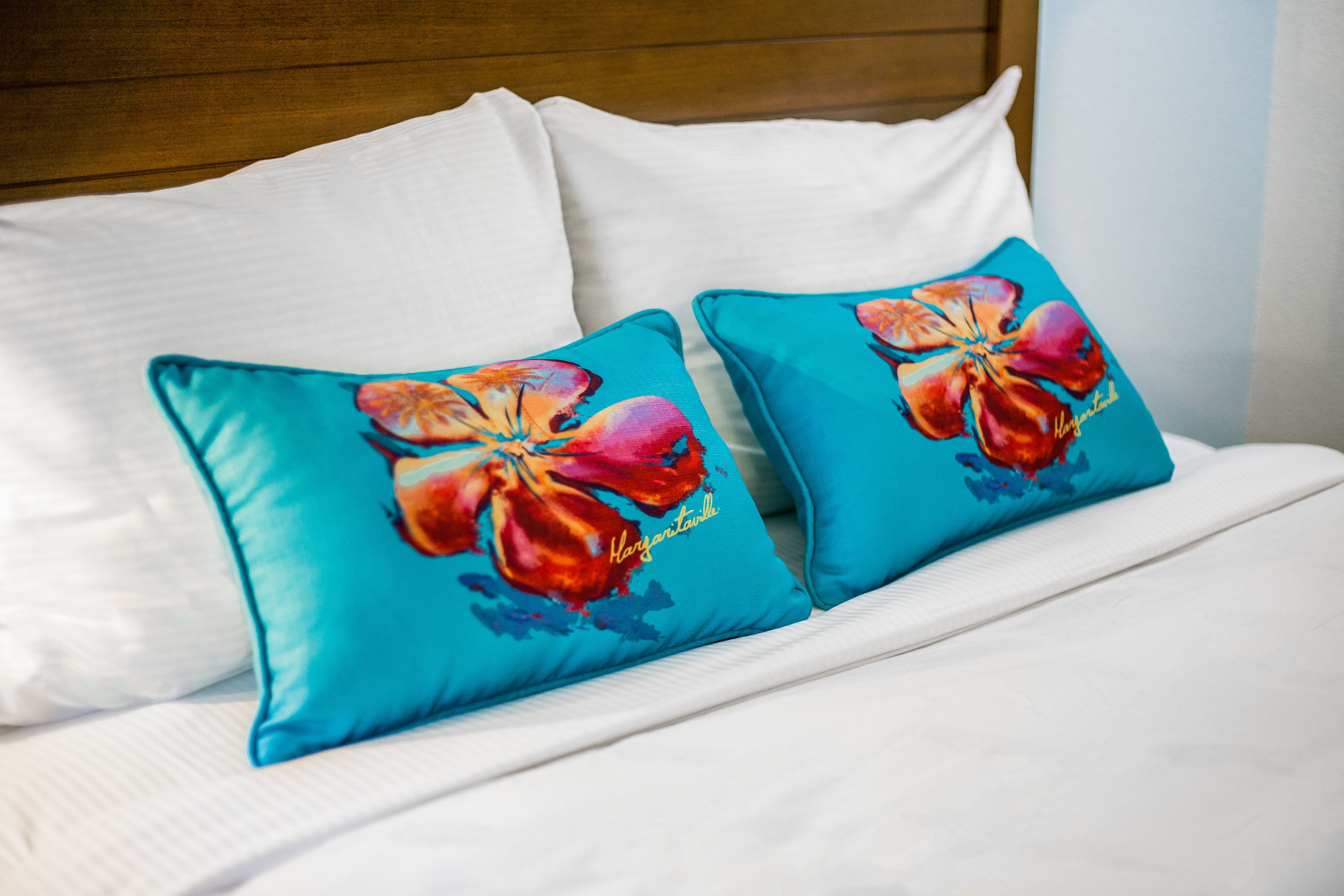 Ein Bett mit weißer Bettwäsche und zwei türkisfarbenen Kissen mit Hibiskusmuster.