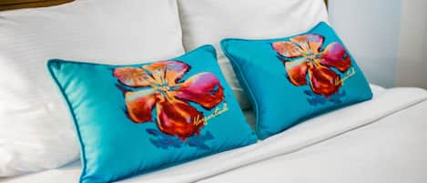 Ein Bett mit weißer Bettwäsche und zwei türkisfarbenen Kissen mit Hibiskusmuster.