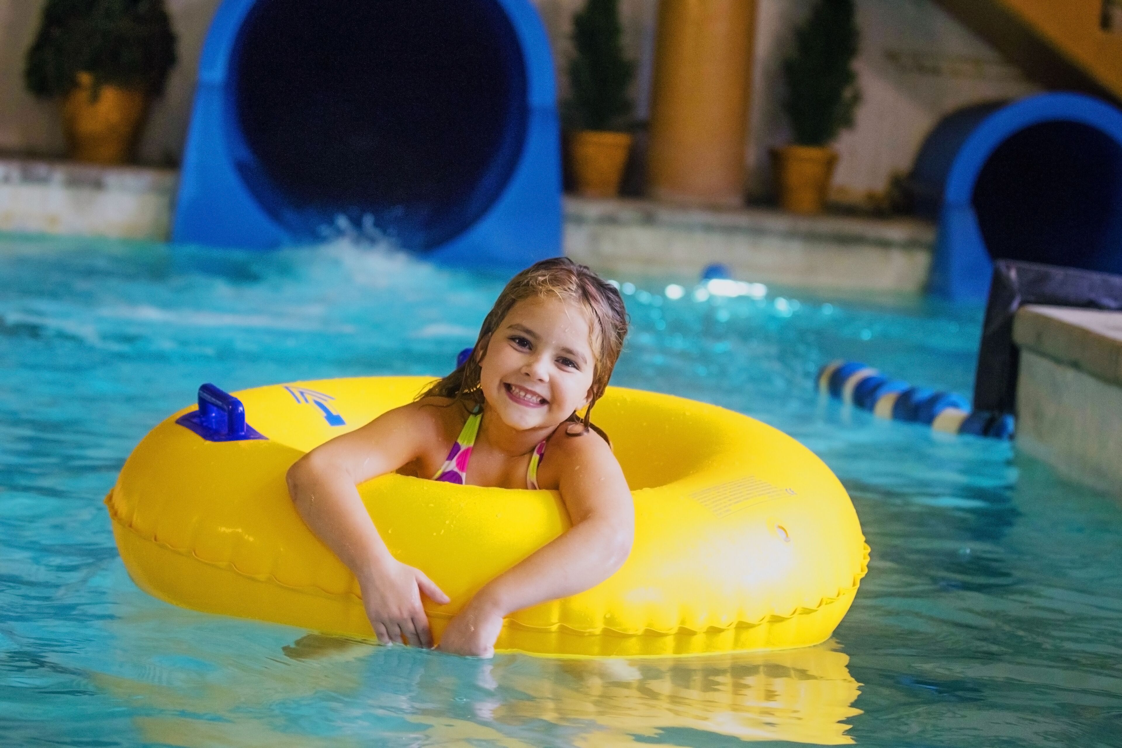 Un enfant dans une piscine, avec un flotteur jaune en forme de cercle.