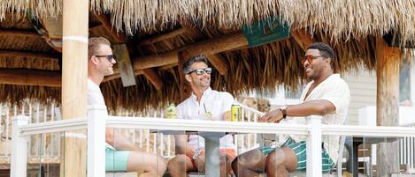 A wooden deck with a thatched roof, seating areas, and a view of the beach.