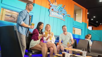 A group of people sitting at tables in a bowling alley with a neon sign reading "Fin City Bowling".