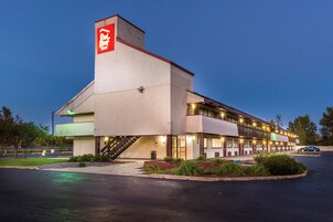 Un hotel Red Roof con un letrero rojo llamativo, una zona exterior cubierta y un estacionamiento.