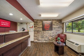 Een receptie met een Red Roof Inn bord, een Red Roof logo, een Red Roof Plus bord en een Red Roof Rewards bord.