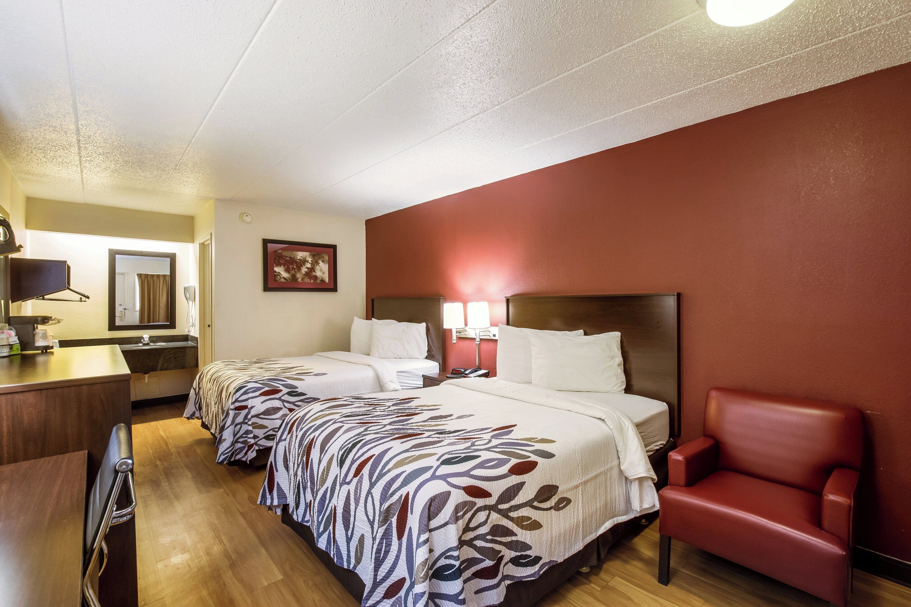 Habitación de hotel con dos camas, un escritorio, una silla y un baño visible a través de una puerta abierta.