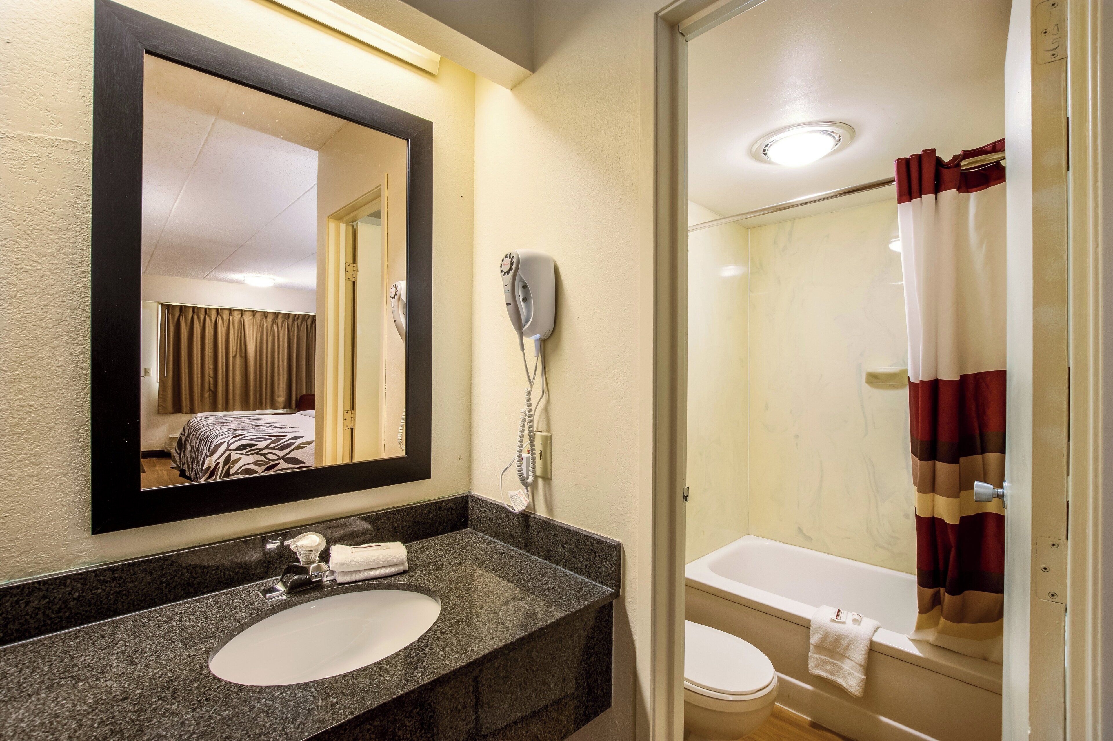 Une salle de bain d’hôtel équipée d’un lavabo en granit, d’un sèche-cheveux, de toilettes et d’une douche avec rideau.
