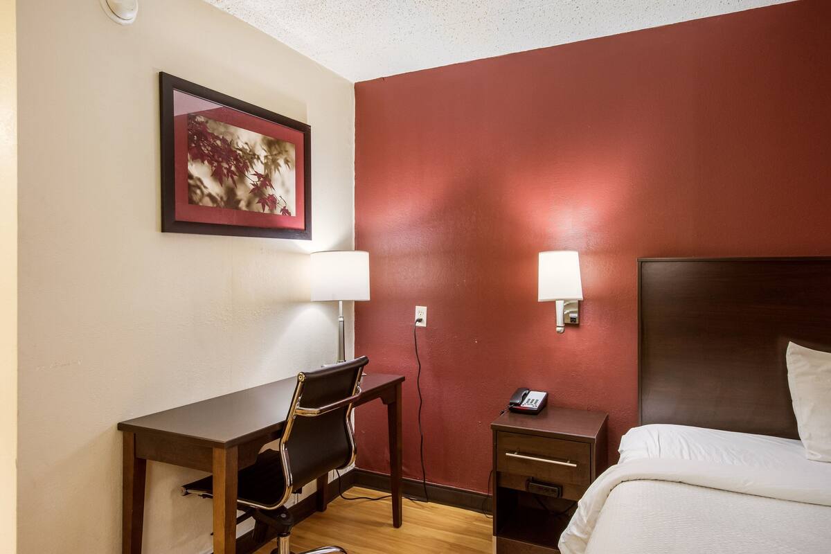 Una habitación de hotel con cama, escritorio, silla y teléfono en la pared.
