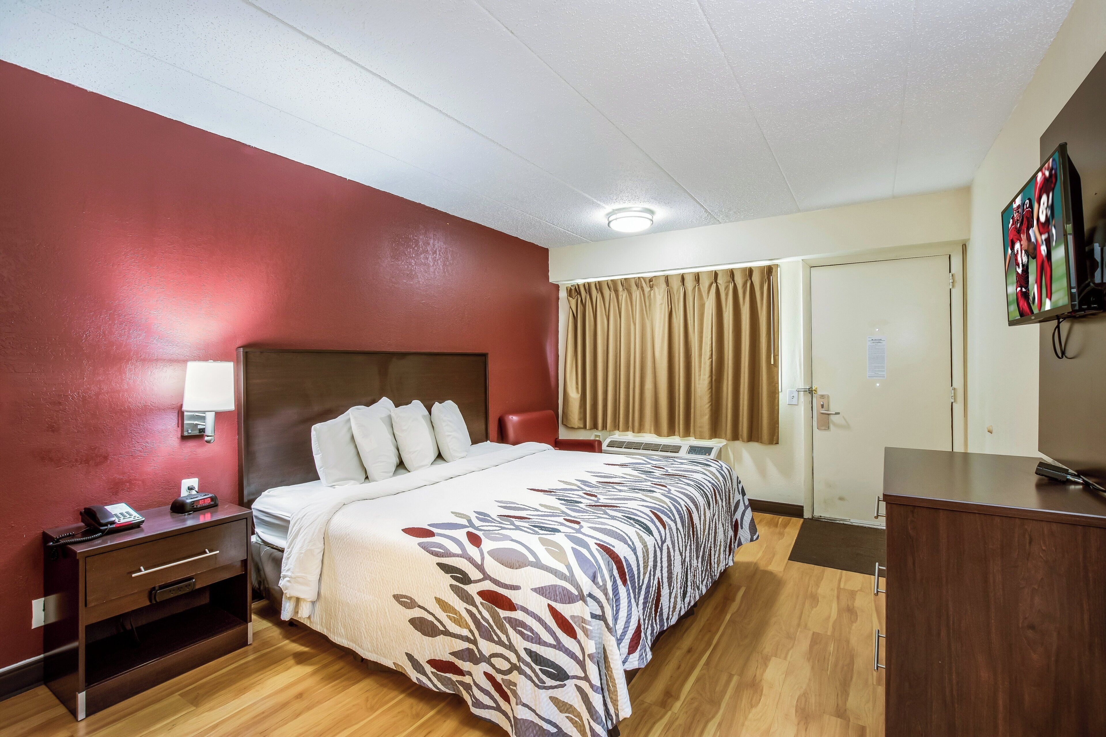 A hotel room with a bed, bedside table, lamp, and a television on a stand.