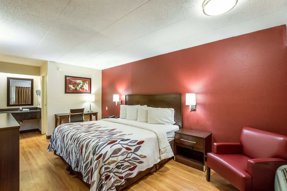 Habitación de hotel con cama, escritorio, silla y sofá rojo.