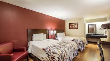 Ein Hotelzimmer mit zwei Betten, einem roten Sessel, einem Schreibtisch mit Spiegel und einem kleinen Badezimmer.