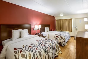Ein Hotelzimmer mit zwei Betten, jeweils mit einem gemusterten Bettüberwurf, einem hölzernen Kopfteil, Nachttischlampen und einer Tür mit Vorhang.